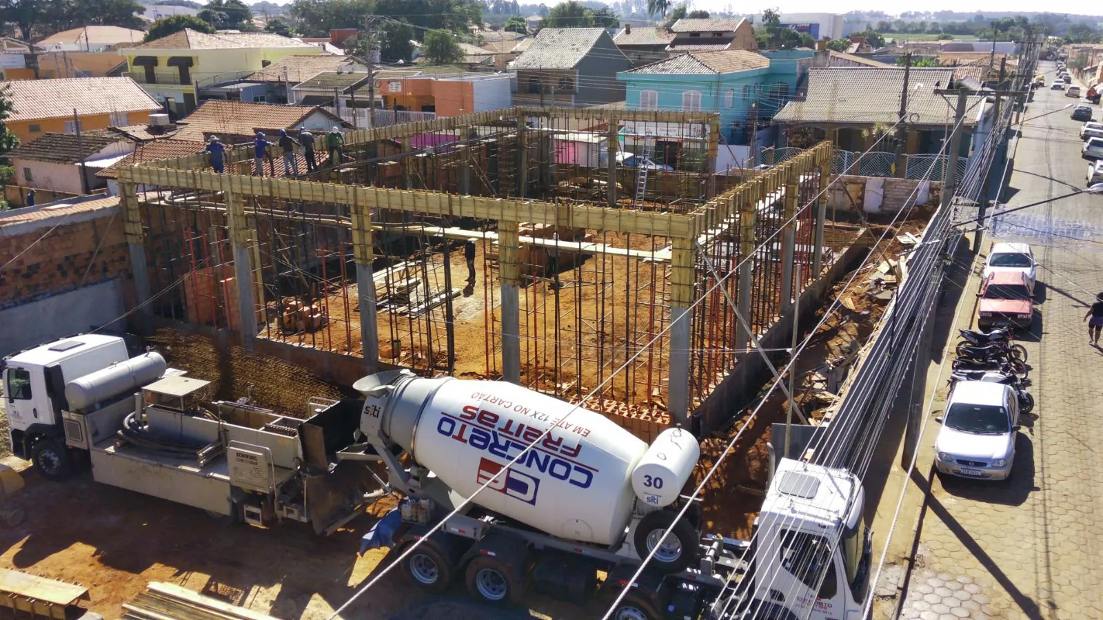 Vista aérea de uma estrutura em concretagem em área urbana, com caminhão betoneira e bomba
